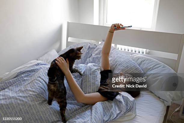 a teenage girl lying in bed looking up as she takes a selfie on her mobile phone. - couch potato expressão em inglês - fotografias e filmes do acervo
