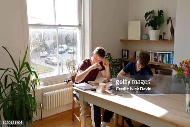 2 teenage boys working and studying together at home sitting at the kitchen table.