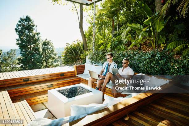 gay couple working on laptop and digital tablet in backyard - sunny backyard stock pictures, royalty-free photos & images
