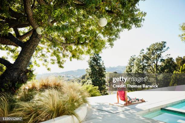 woman performing yoga on pool deck of home - woman yoga trees ストックフォトと画像
