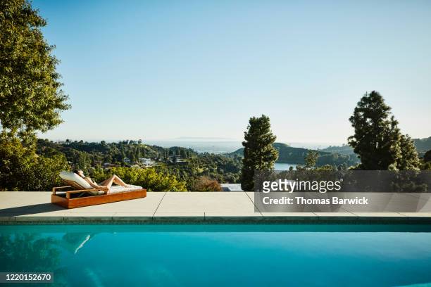 woman relaxing in lounge chair at edge of pool - waters edge photos et images de collection