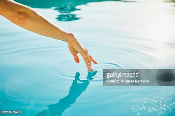 womans hand touching surface of water - touching photos et images de collection