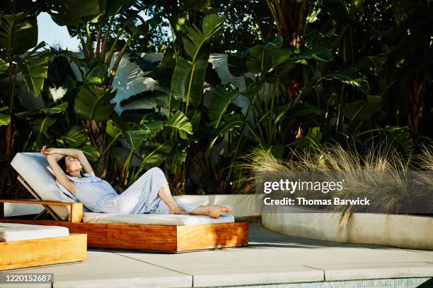 woman relaxing in lounge chair on pool deck - sdraio da spiaggia foto e immagini stock