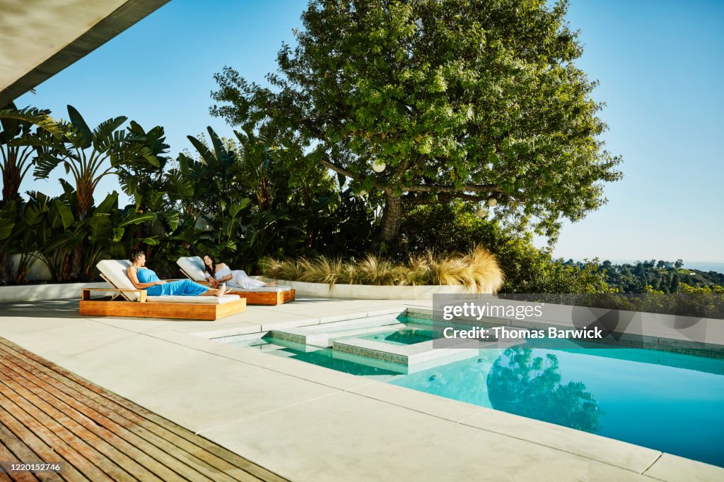 Female friends in discussion while relaxing in lounge chairs by pool