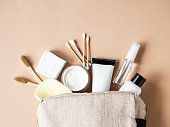 Travel cosmetic bag with the necessary means to care for women's skin. Cosmetics, dry shampoo, cotton buds, toothbrushes next a cosmetic bag on a beige background. top view