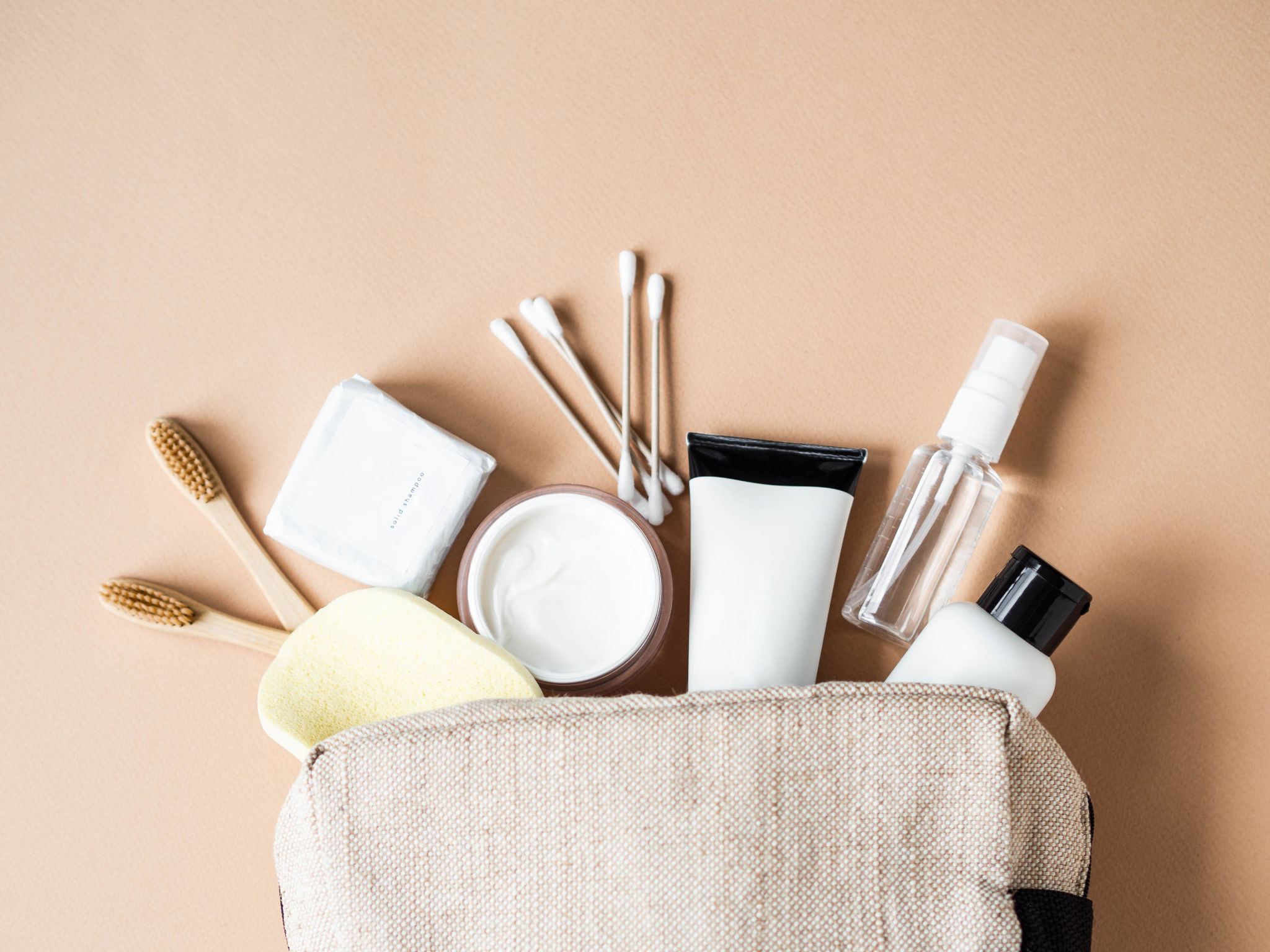 Travel cosmetic bag with the necessary means to care for women's skin. Cosmetics, dry shampoo, cotton buds, toothbrushes next a cosmetic bag on a beige background. top view Travel cosmetic bag with the necessary means to care for women's skin. Cosmetics, dry shampoo, cotton buds, toothbrushes next a cosmetic bag on a beige background. top view