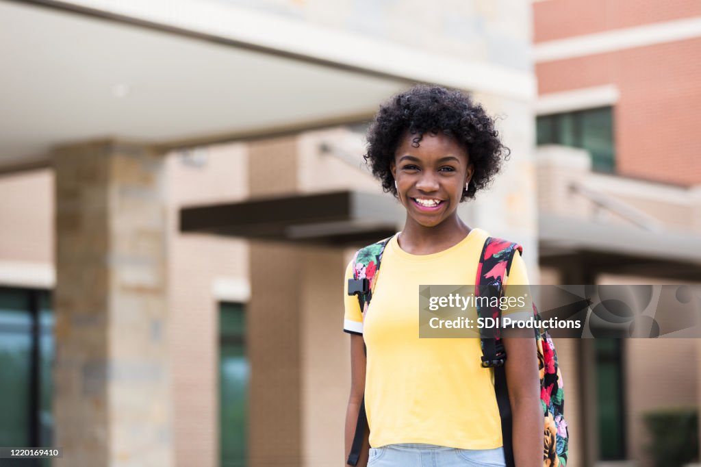Feliz niña de la edad de la escuela media se para frente a la escuela