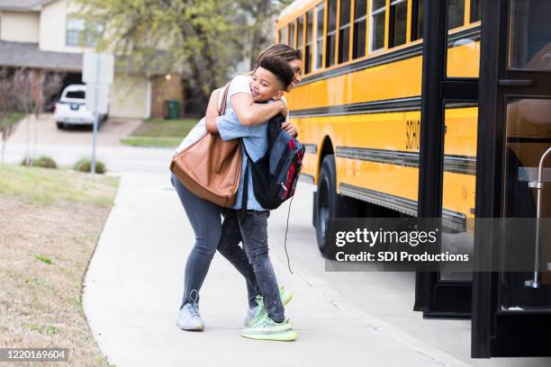 mom greets elementary age son at bus stop - first day school hug stock pictures, royalty-free photos & images