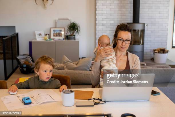 a mom trying to work from home while holding her daughter and watching her son during the covid-19 home quarantine. - working mom stock pictures, royalty-free photos & images