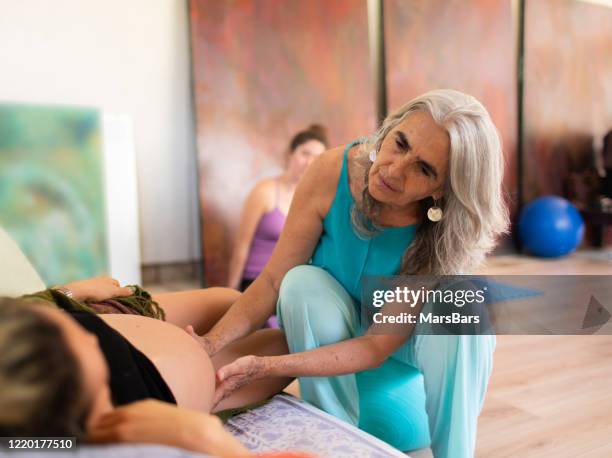 hermosa doula madura con el pelo gris examina a una mujer embarazada - comadrona fotografías e imágenes de stock