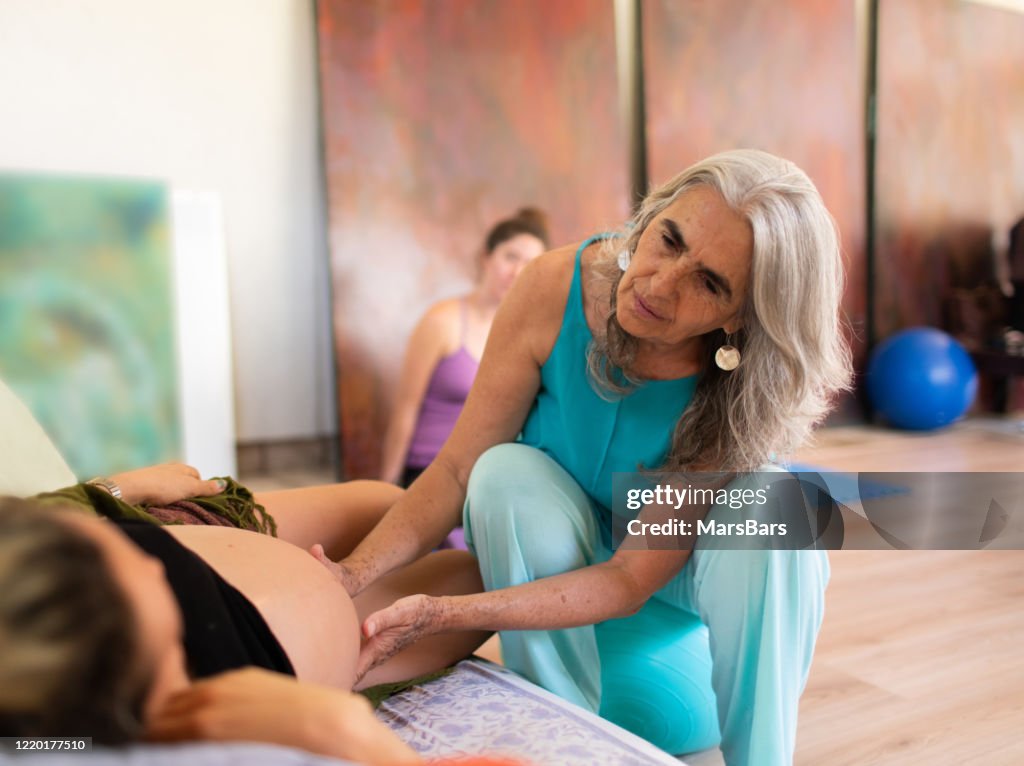 Vacker mogen doula med grått hår undersöker en gravid kvinna