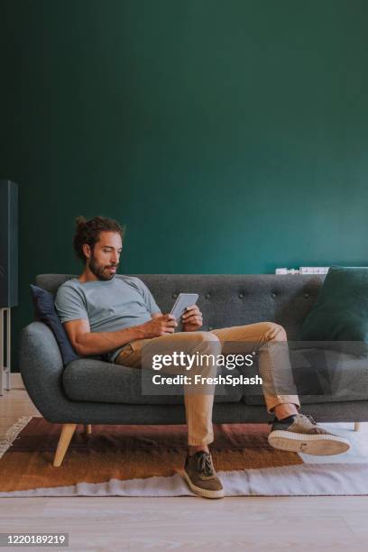 hombre sentado en un sofá y usando una tableta digital en casa - man sitting on sofa fotografías e imágenes de stock