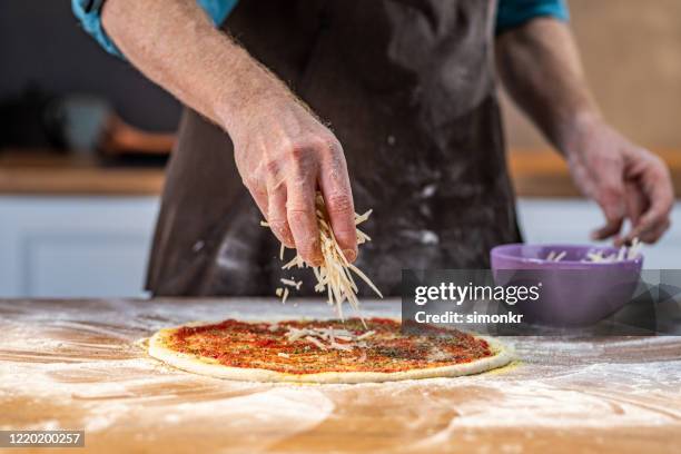 chef adding grated cheese on dough - grated cheese stock pictures, royalty-free photos & images