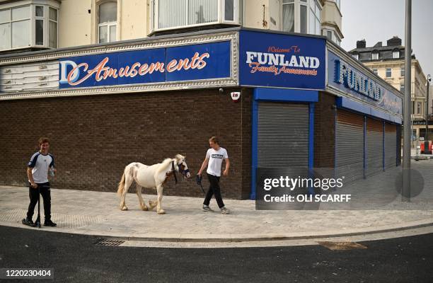 Man walks with a pony past an amusement arcade, still closed-down down due to the COVID-19 pandemic, in Bridlington on the north east coast of...