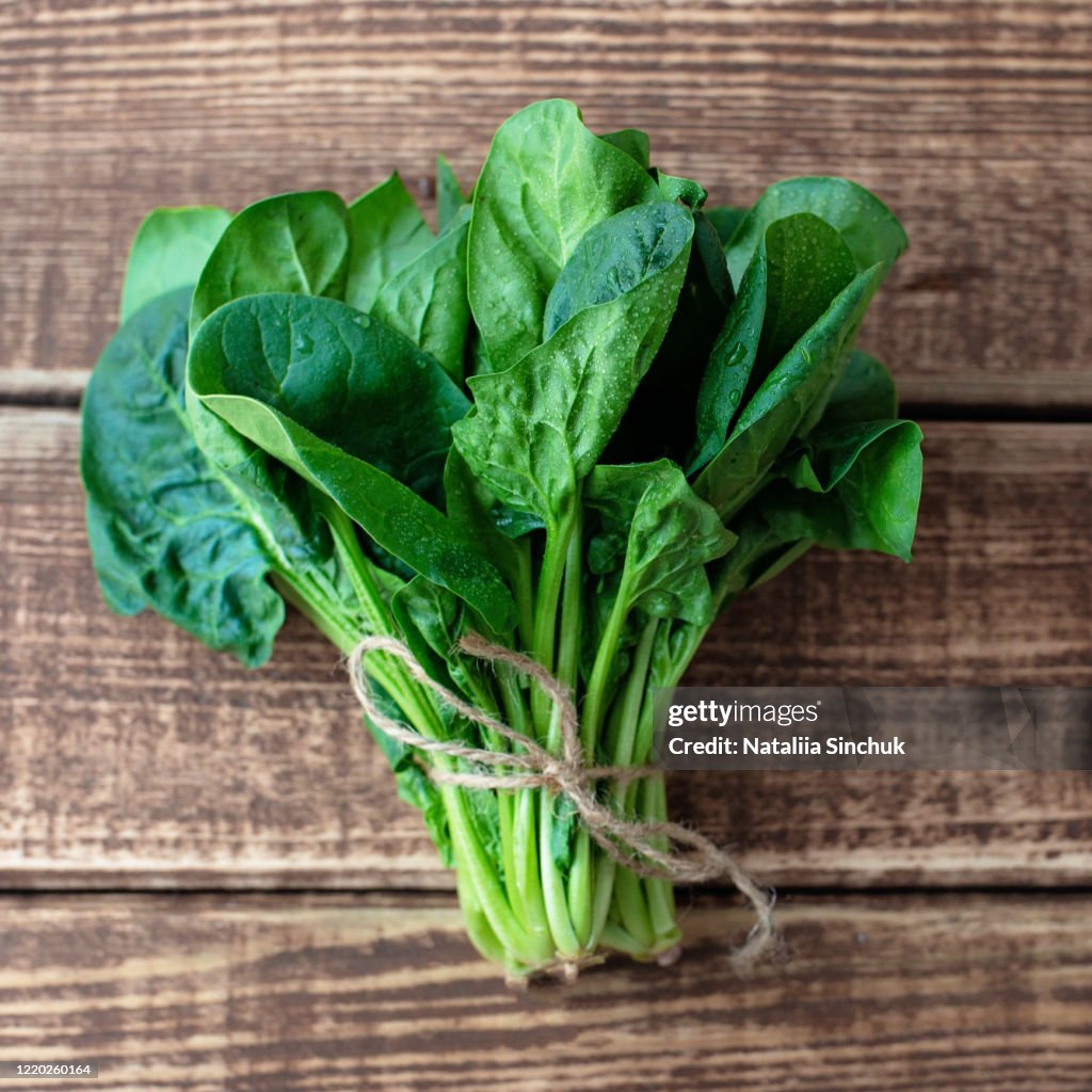 Clean food concept. Leaves of ripe juicy freshly picked organic spinach greens on a wooden background. Healthy detox spring-summer diet. Vegan Raw Food.