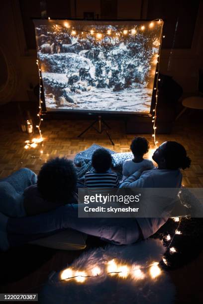 por encima de la vista de la familia negra viendo una película en la pantalla de proyección en casa. - familia viendo tv fotografías e imágenes de stock