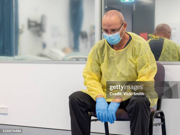 male health care sitting in a chair beside a closed hospital room looking exhausted - coronavirus australia stock-fotos und bilder