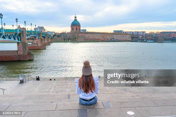 asian woman sitting garonne river and dome de la grave in toulouse, france - south of france stockfoto's en -beelden