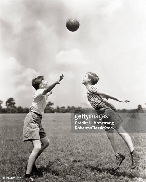 1930s two boys in grass playing soccer ball in air between them