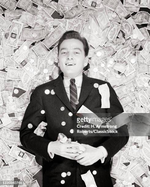1950s smiling man lying on back on a pile of money coins and bills looking at camera winner lucky lottery prize money