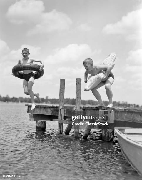 1940s 1950s two boys wearing inflatable inner tubes about to jump in lake off pier