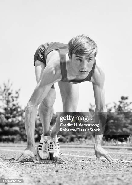 1960s head on view teenage man athlete track runner in starting block in crouching position ready for race