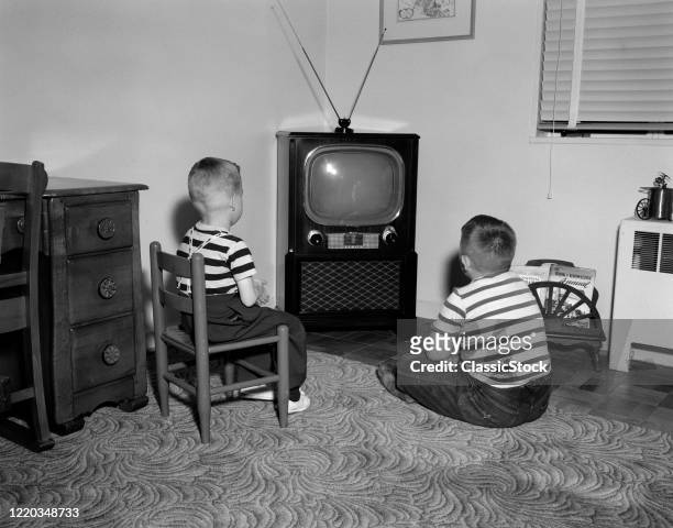 1950s TWO BOYS SITTING IN LIVING ROOM WATCHING TELEVISION