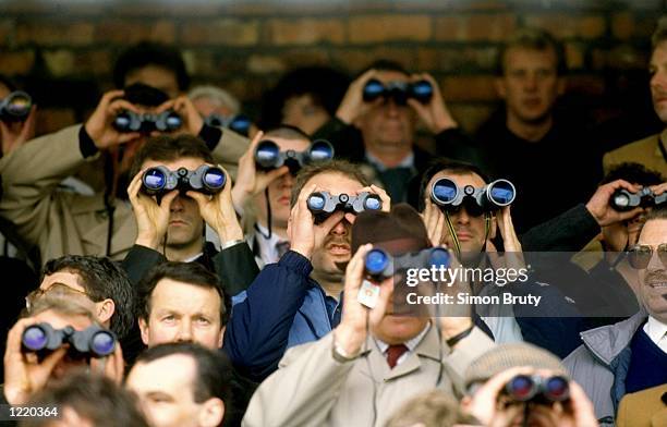 General view of the crowd watching the races through binoculars during the Cheltenham Festival held at Cheltenham Racecourse in Gloucestershire,...