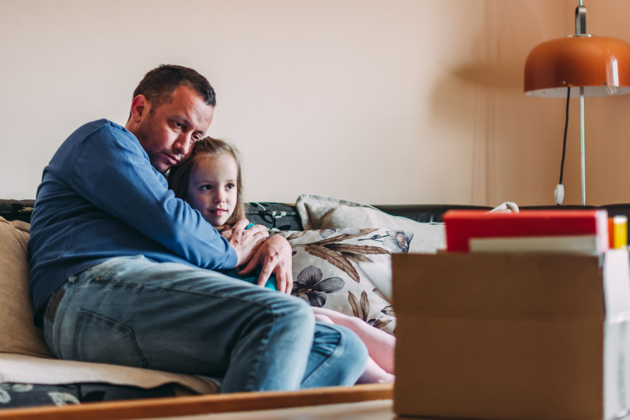 Men sitting on sofa at home and embracing her little daughter after he get fired from a job Men sitting on sofa at home and embracing her little daughter after he get fired from a job