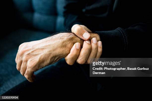 a man holding his wrist, feeling pain - menschlicher arm stock-fotos und bilder