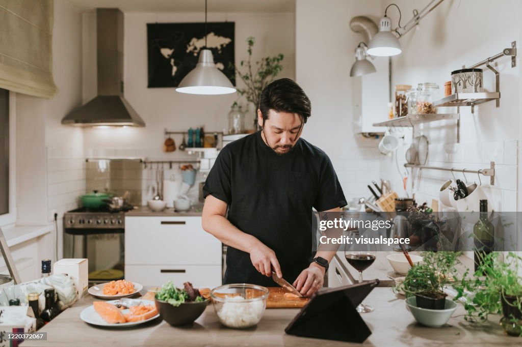 Japanese man cuts fresh salmon while looking at digital tablet