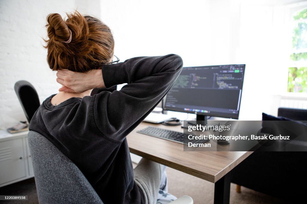 A woman holding her neck while working on computer sitting at desk at home