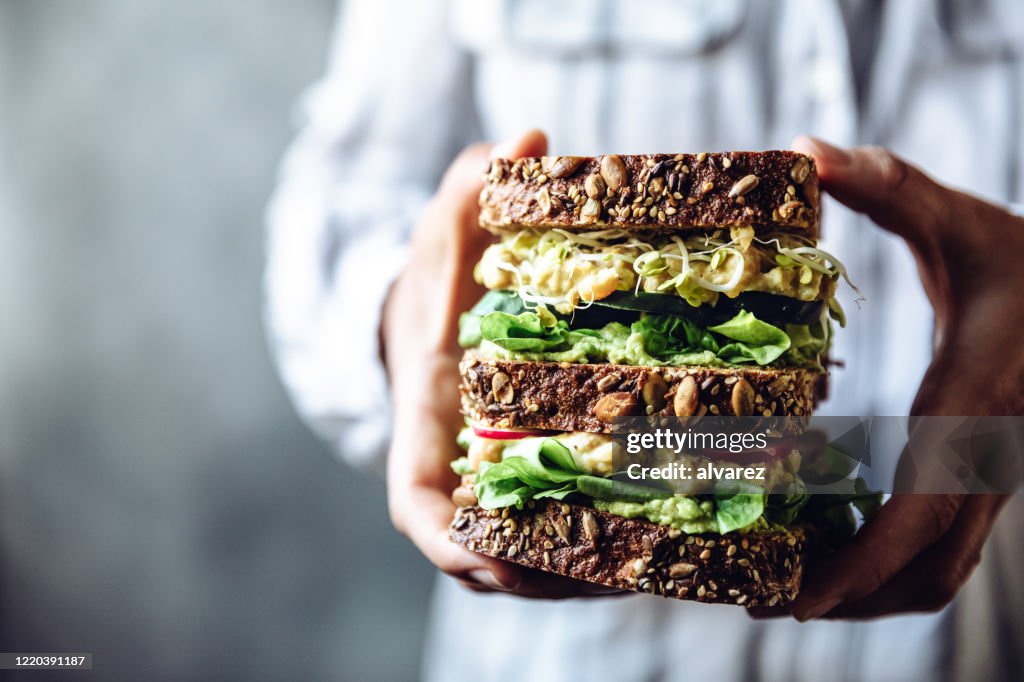 Kvinnans händer håller en stor vegetarisk smörgås