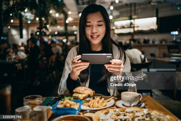 smiling young woman taking photo of freshly served food on the dining table with mobile phone during meal in a western restaurant - bar local de entretenimento imagens e fotografias de stock