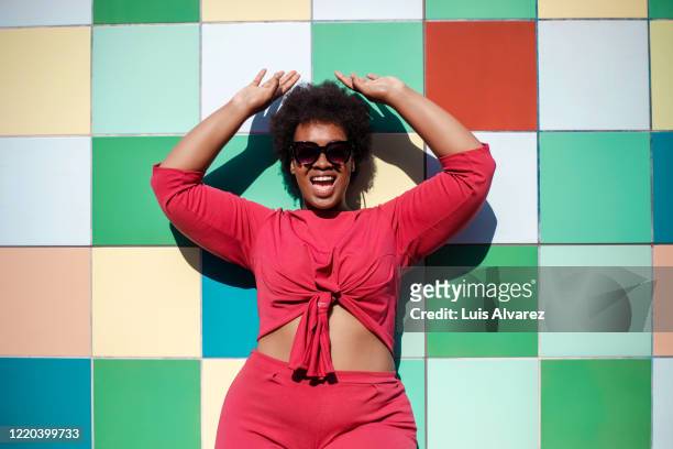 stylish woman looking excited against multicolored tiled wall - afro hairstyle stock-fotos und bilder
