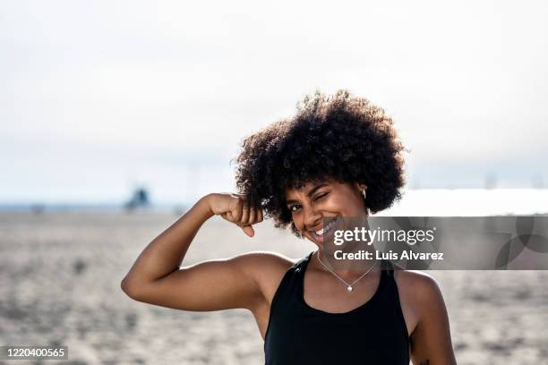 fit woman on the beach flexing her biceps - strength training stock-fotos und bilder