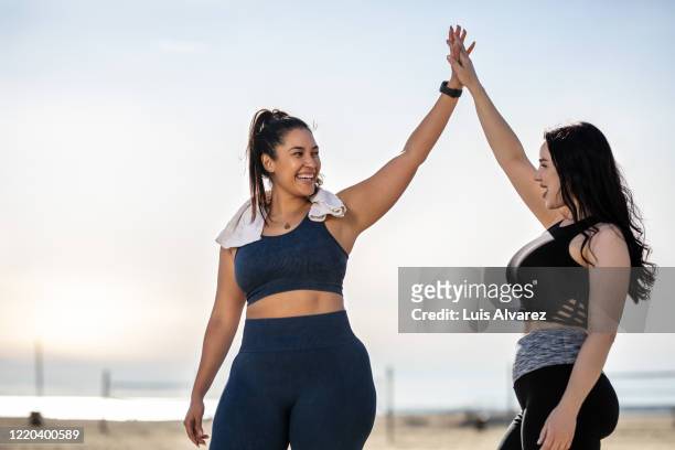 women giving each other a high five after exercising at the beach - abspecken stock-fotos und bilder