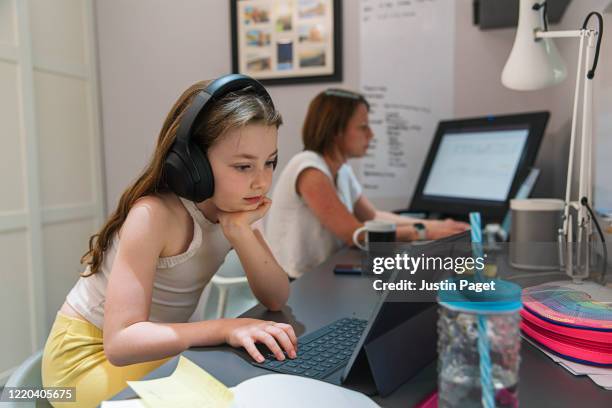 young girl remote schooling in study. mother is working in the background - mutter tablet zuhause stock-fotos und bilder