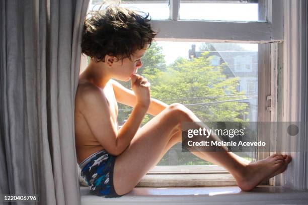 little boy with brown curly hair sitting curled up in a window sill.  he is framed by the window and curtains on either side of him. the light from outside is streaming in around him making shapes on him, and the boy is in shadow. - kids in undies stock pictures, royalty-free photos & images