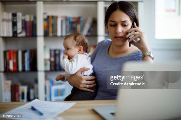 worried mother using mobile phone an laptop at home - pandemic illness stock pictures, royalty-free photos & images