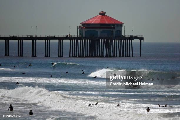 Surfers ride waves in front of the Huntington Beach pier on the beach on April 22, 2020 in Huntington Beach, California. Southern California is...