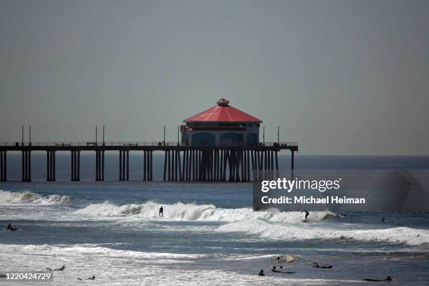 Surfers ride waves in front of the Huntington Beach pier on the beach on April 22, 2020 in Huntington Beach, California. Southern California is...