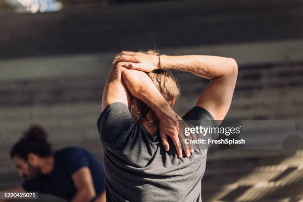 rückansicht eines blonden mannes, der sich für einen city run mit freunden aufwärmt - rückentraining stock-fotos und bilder