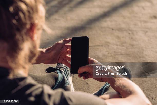 over the shoulder view of a runner using a smartphone outdoors (blank screen, copy space) - text message screen stock pictures, royalty-free photos & images