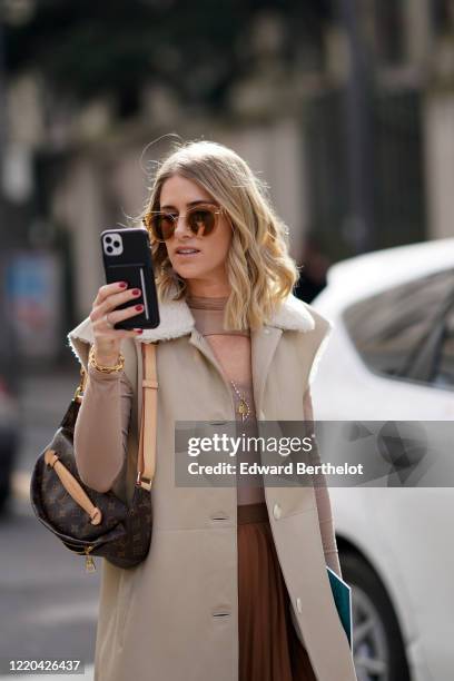 Guest wears a hair brooch, a beige long sleeveless coat, a brown leather monogram Vuitton fanny pack bag, sunglasses, outside Sportmax, during Milan...