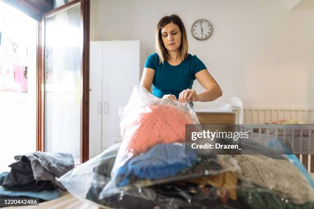 frau räumt den schrank auf und sortiert kleidung in vakuumbeuteln - zuhause-bleiben-anordnung stock-fotos und bilder