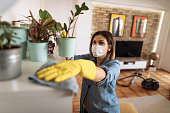 Woman wiping dust from shelf and other furniture in living room