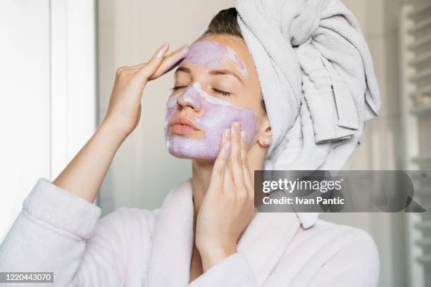 portret van jonge mooie vrouw met een gezichtsmasker dat een kuuroordbehandeling thuis heeft - face pack stockfoto's en -beelden