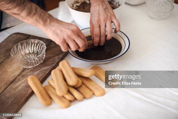 cucina in quarantena: un uomo sta immergendo ladyfinger-biscotti nel caffè per preparare il tiramisù - tiramisù foto e immagini stock