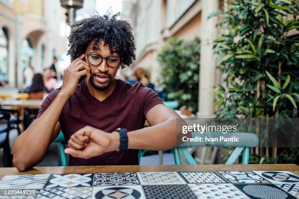 jonge afrikaanse amerikaan die van zijn vrije tijd in openlucht geniet - african american restaurant texting stockfoto's en -beelden
